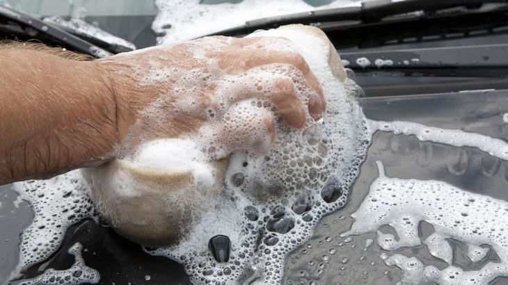 a hand holding a soapy sponge washing a black car
